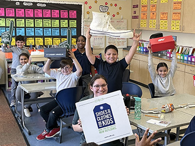 Happy Kids in classroom holding sign of Shoes and Clothes for Kids