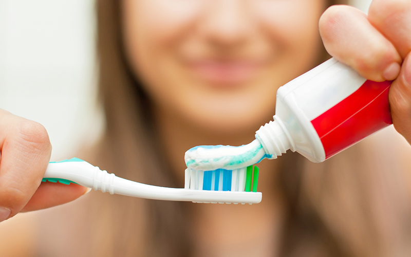 Toothbrush with toothpaste Young woman holding a toothbrush and placing toothpaste on it.